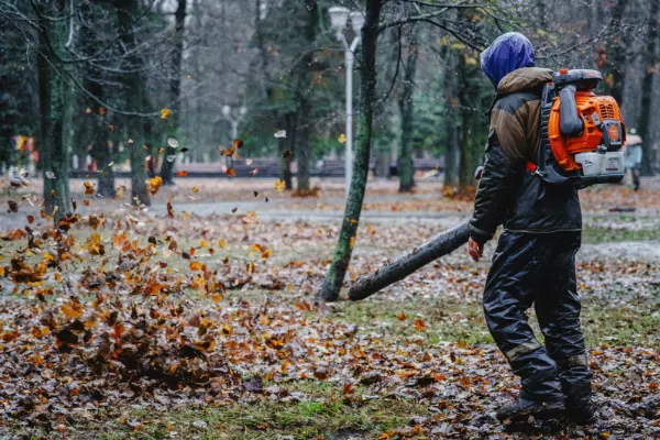 Radnik leđnim puhačem čisti lišće sa staze u parku