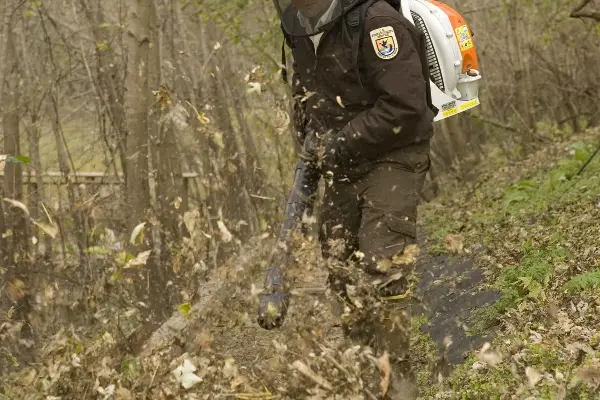 Radnik s leđnim puhačem čisti lišće sa staze