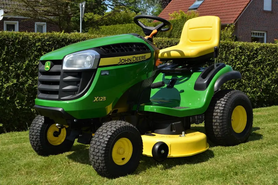 Traktor kosilica ispred kuće, uz živicu